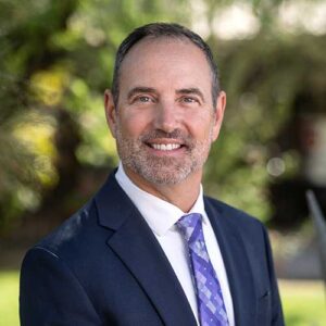 Photo of Chip Beard - a smiling man wearing a suit in front of a backdrop of trees in soft focus