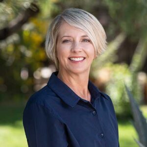 Photo of Michelle Adamczyk - a smiling woman with short hair in front of a backdrop of trees in soft focus